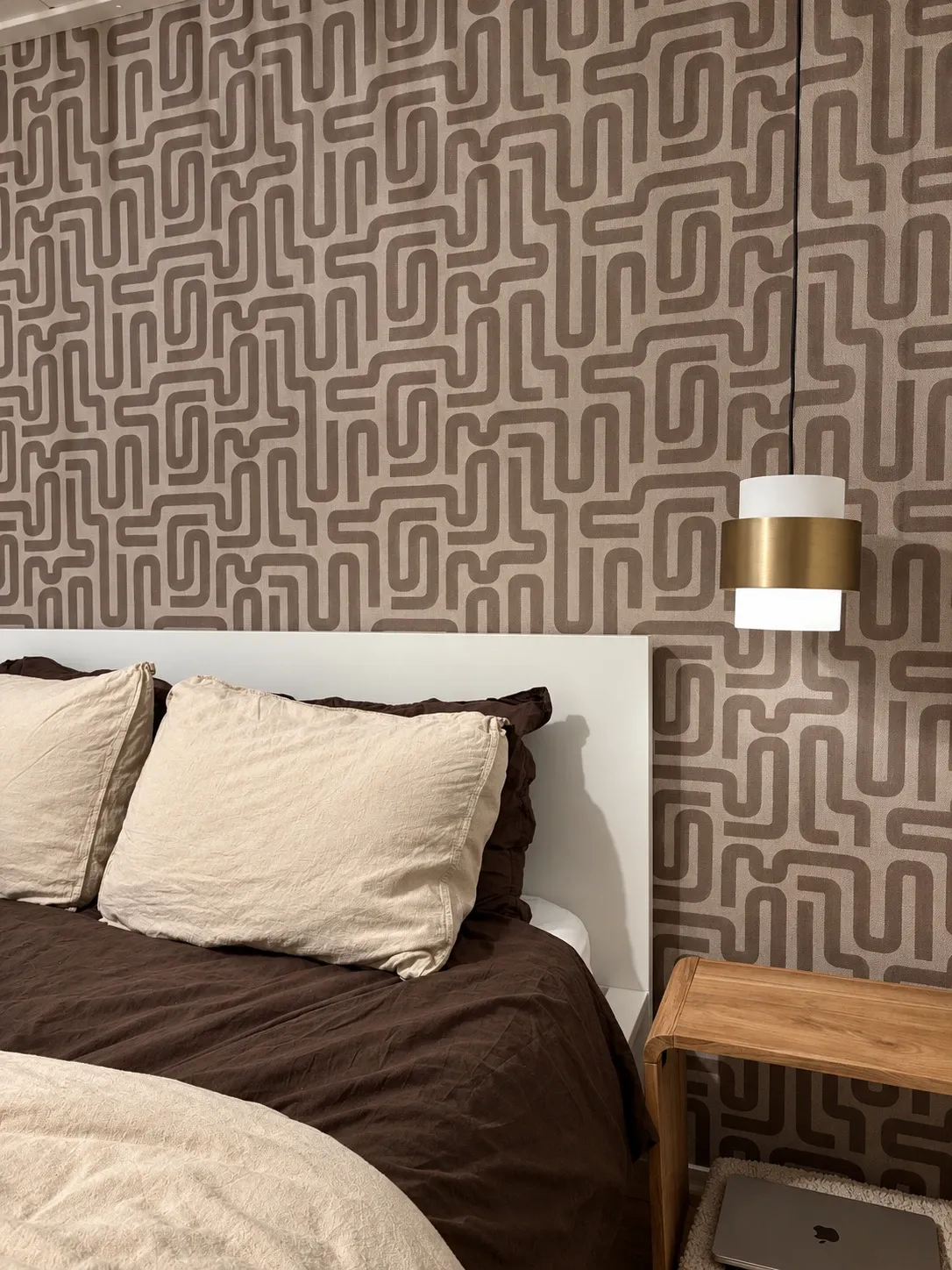 Bed met linnen kussens voor grafisch behang, messing hanglamp en eiken nachtkastje